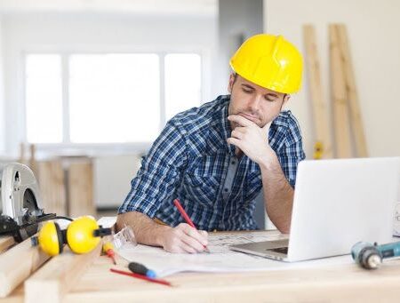 ingener stel инженер СТЭЛ в клетчатой рубашке и каске за ноутбуком производит расчеты